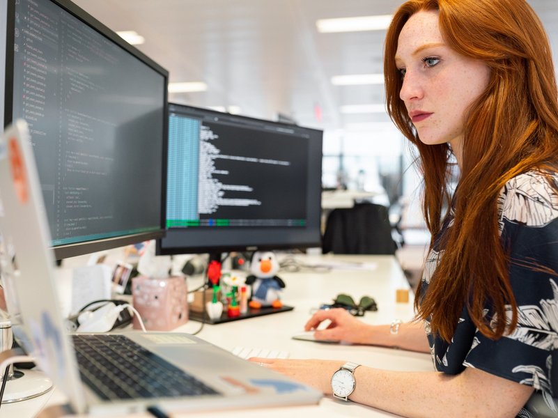 Eine Studentin sitzt vor drei Monitoren und erledigt Programmierarbeiten.