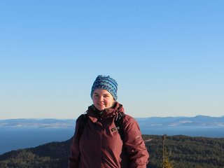 Studentin in norwegischer Schneelandschaft, blauer Himmel, Wald im Hintergrund.