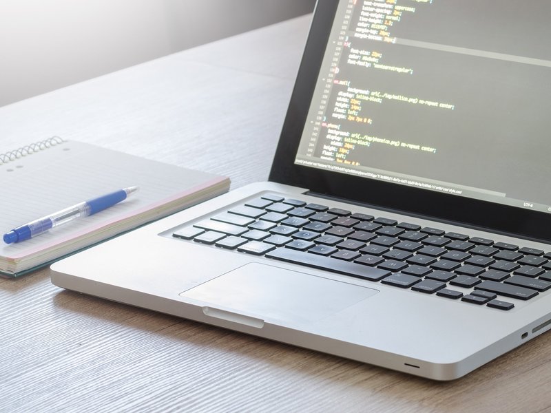 Ein Laptop auf einem Tisch, daneben Schreibblock und Stift